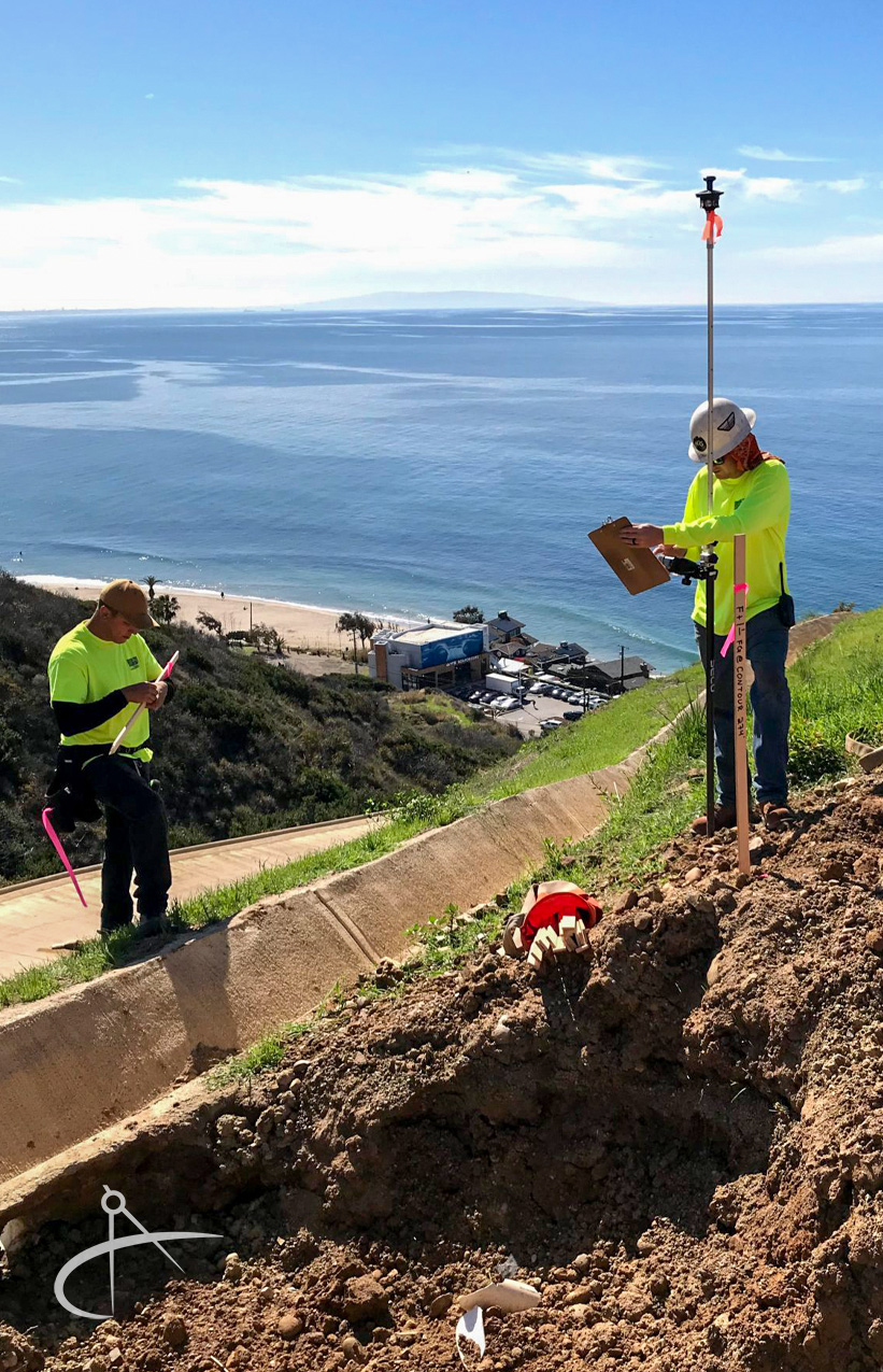 Two surveyors setting stakes near the Pacific Ocean.